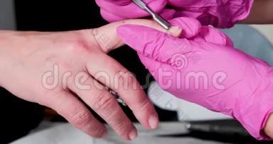 美甲师傅在粉红色手套上用电钻刮掉美甲沙龙的旧清漆。 美容专业美甲